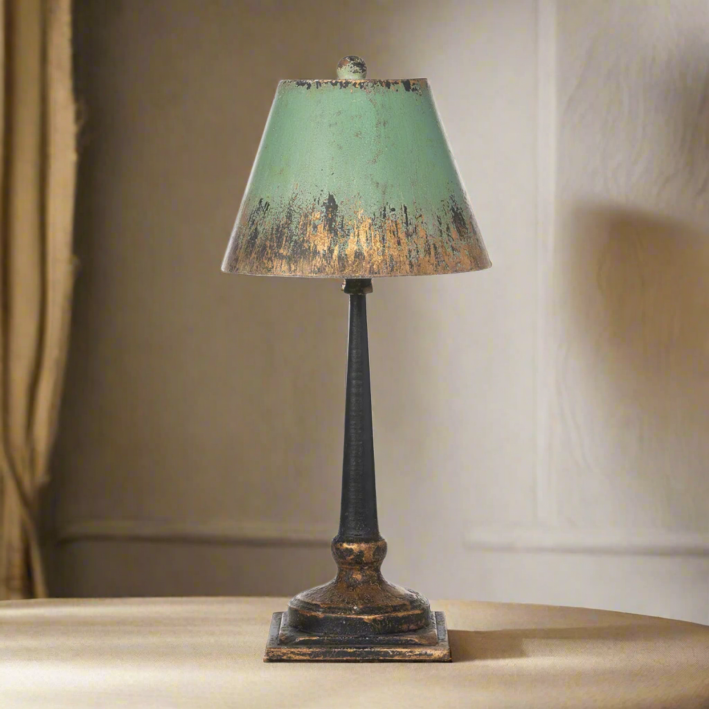 Vintage table lamp with distressed green and gold shade, exuding nostalgic charm atop a textured bronze and golden base.