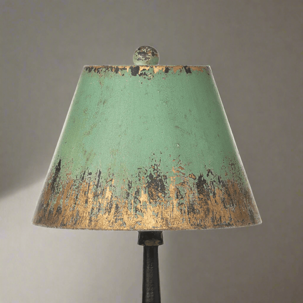 Vintage table lamp with distressed green and gold shade, exuding classic elegance and nostalgic charm.