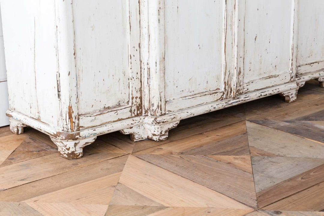 Vintage white entryway cabinet with distressed wood top on rustic floor in country cottage style.