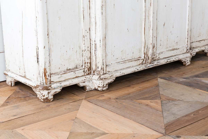 Vintage white entryway cabinet with distressed wood top on rustic floor in country cottage style.