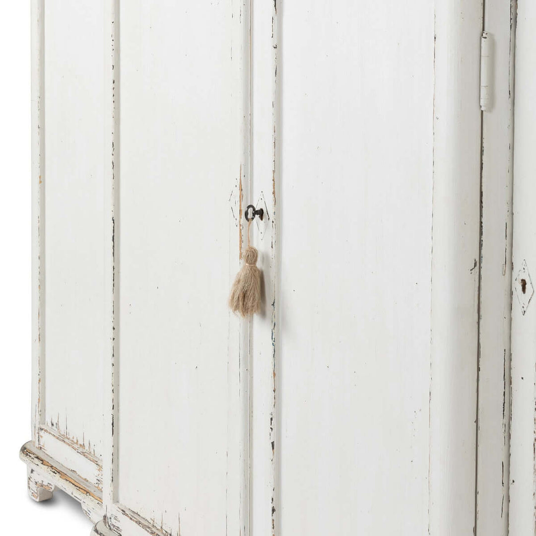 Vintage white painted entryway cabinet with distressed wood top and tassel detail, evoking a cozy, cottage-style ambiance.