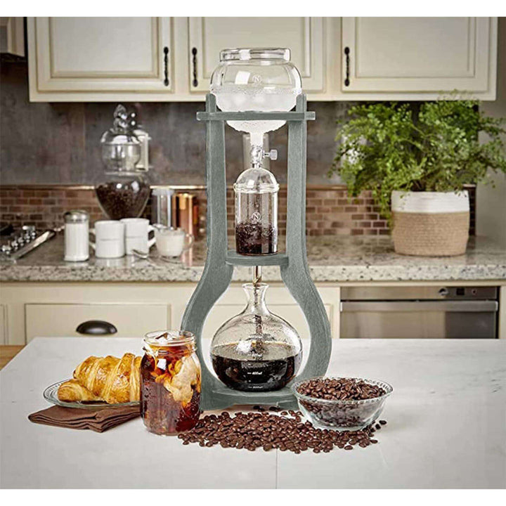Vintage Wooden Cold Brew Coffee Maker Tower on kitchen counter with glass vessels, surrounded by coffee beans and croissants.