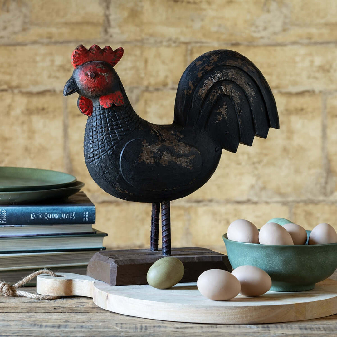 Vintage Wooden Rooster Statue on a rustic table setting with eggs, showcasing folk art charm in antique black and barn red.