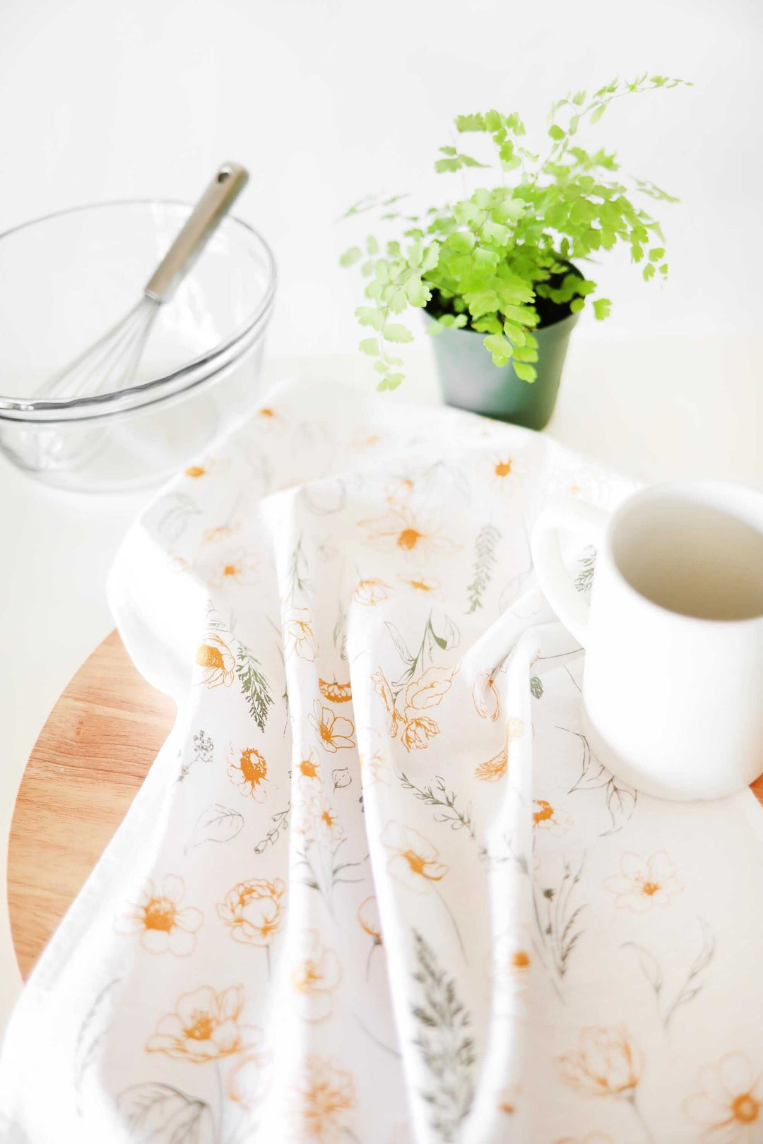 Vintage Botanical Flower Garden Tea Towel with watercolor floral print next to whisk, glass bowl, plant, and mug in a bright kitchen.