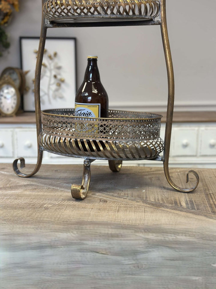 Vintage brass 2-tier metal bar cart stand with ornate detailing and intricate design on a wooden table.