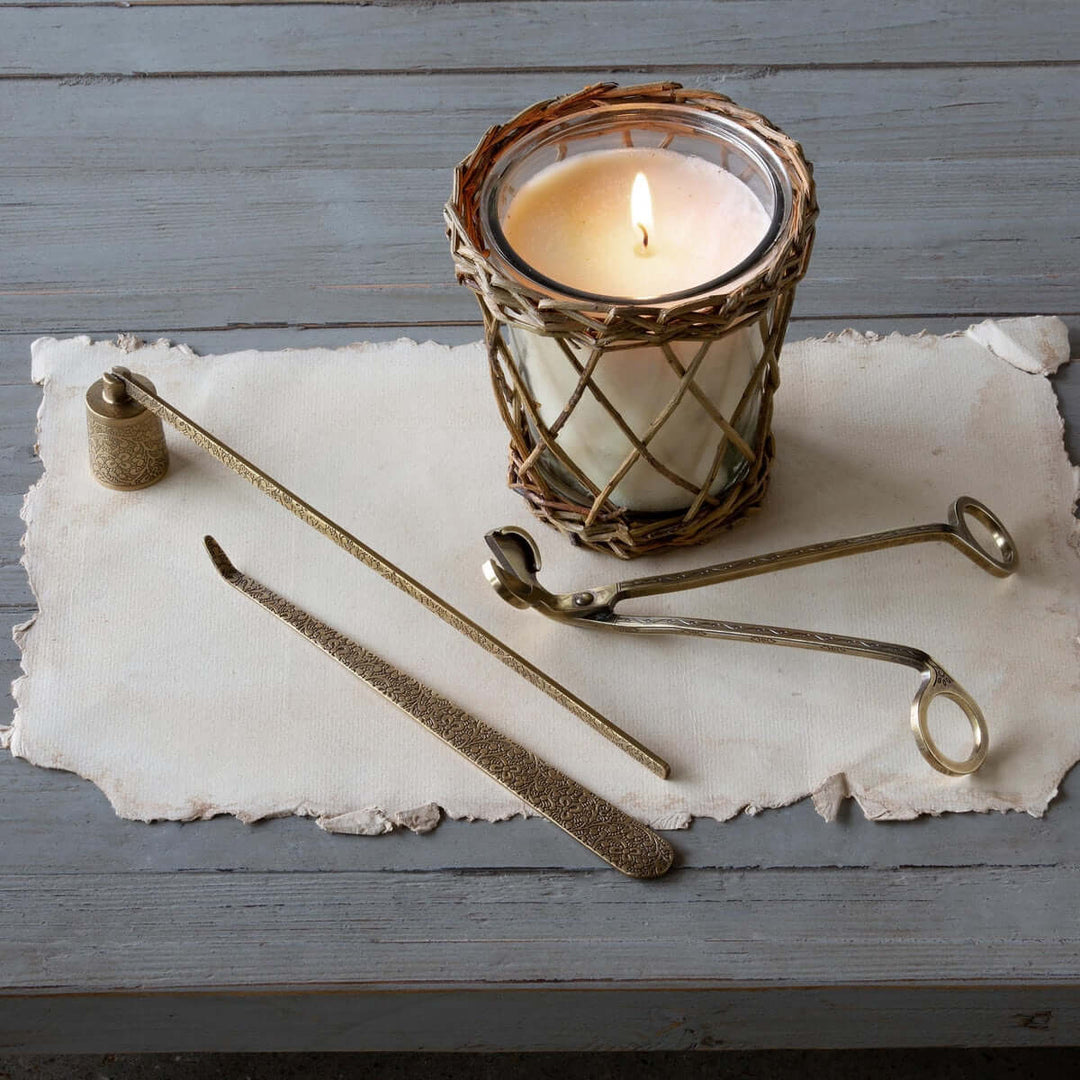 Vintage Brass Candle Care Kit set of 3 with candle burning, on rustic table. Elegant candle maintenance tools with engraved finish.