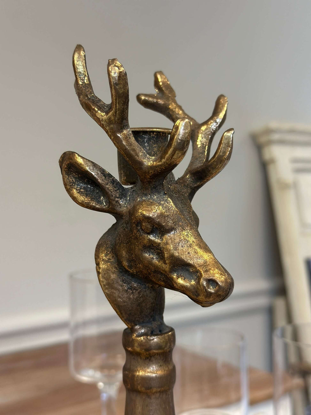 Vintage brass deer head candle holder with sculpted antlers on a turned base, showcasing antique patina in rustic setting.