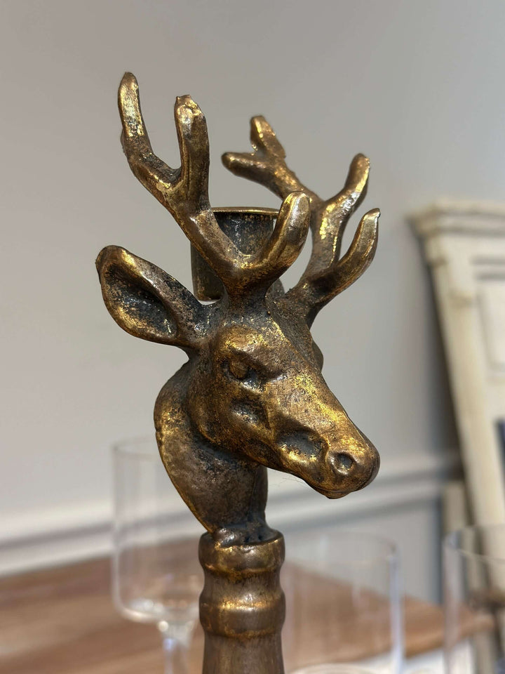 Vintage brass deer head candle holder with sculpted antlers on a turned base, showcasing antique patina in rustic setting.