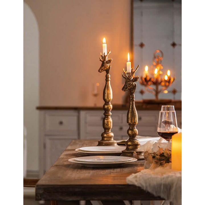 Vintage brass deer head candle holders on a dining table with lit candles casting warm golden glow, creating a rustic, antique ambiance.