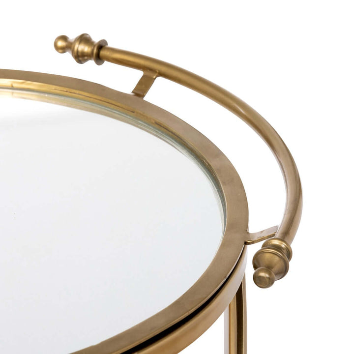 Close-up of a vintage brass round bar cart with mirrored shelf, showcasing elegant Hollywood Regency design.