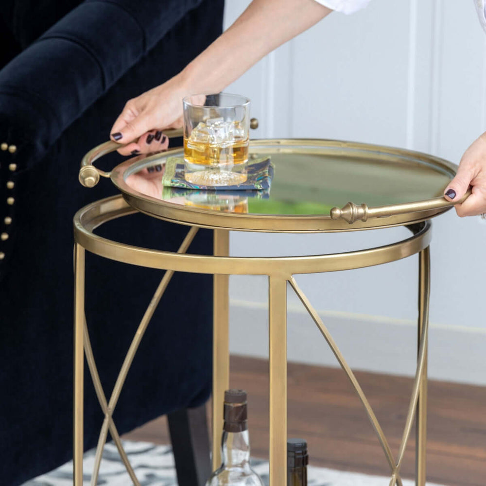 Vintage brass bar cart with mirrored shelves and a glass of whiskey, showcasing Hollywood Regency style elegance.