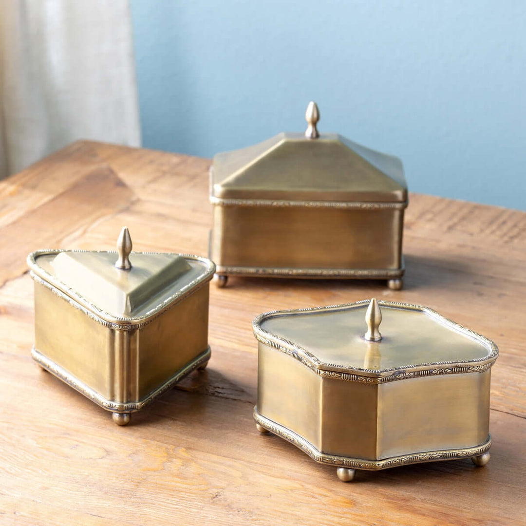 Set of 3 vintage brass trinket boxes with lids, featuring triangle, rectangle, and diamond shapes on a wooden surface.