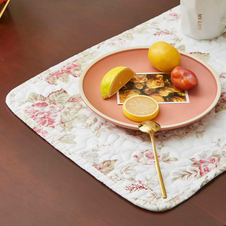 Vintage Cottage Rose Quilted Placemats (Set of 4) with plate and fruit on a wooden table, featuring pink roses and green leaves pattern.
