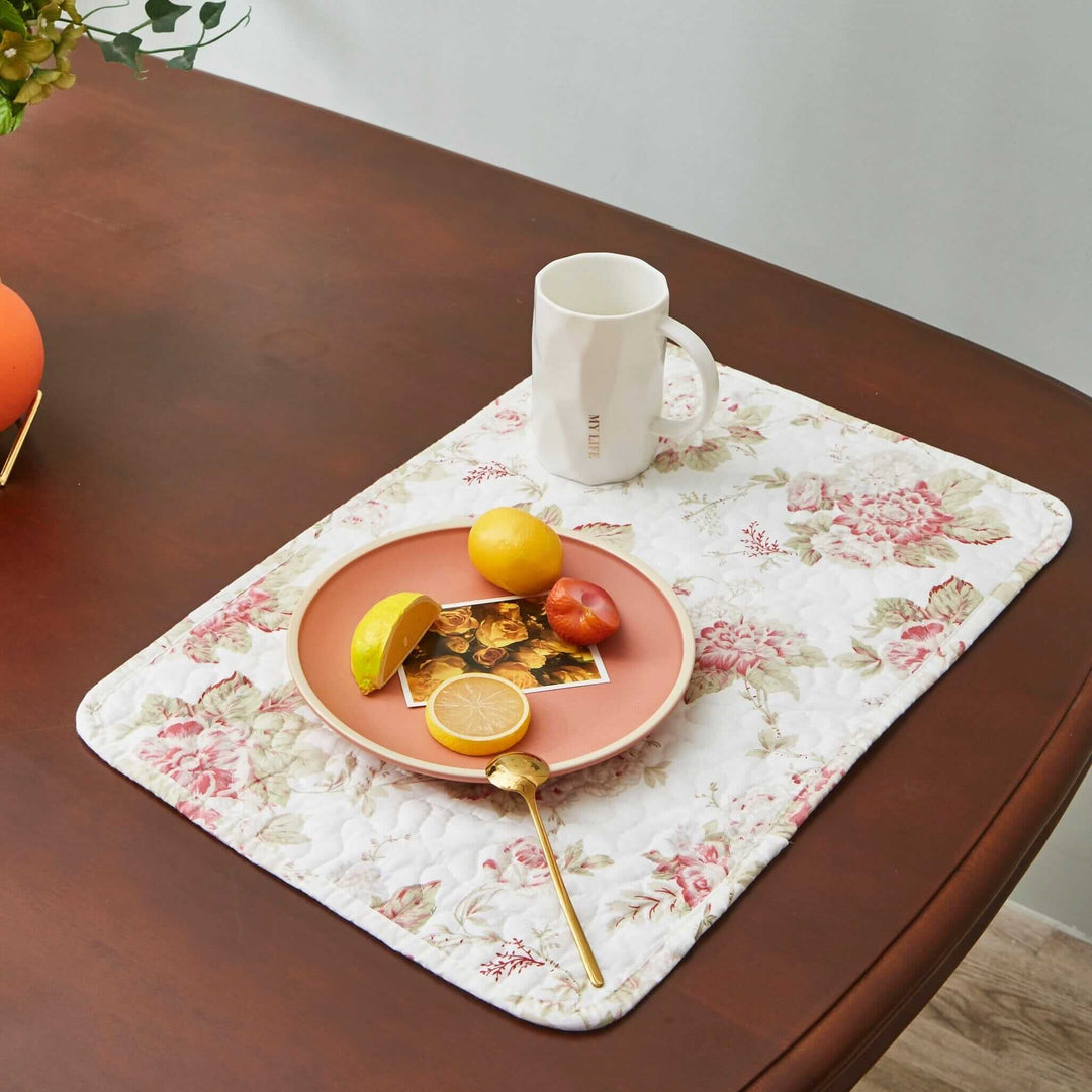 Vintage Cottage Rose Quilted Placemats (Set of 4) on a wooden table with a cup and plate