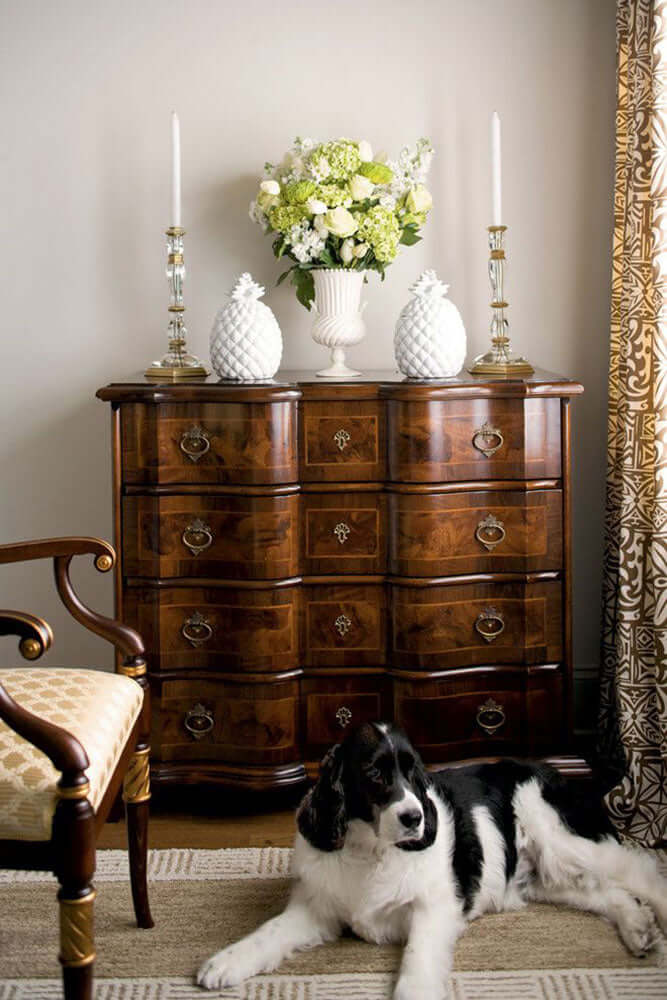 Dog lying on the floor in front of a wooden dresser with decorative items.
