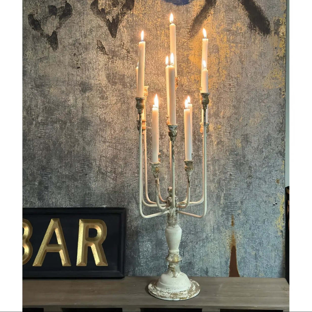 Vintage Farmhouse Candelabra in Distressed White Iron with lit candles against textured wall.