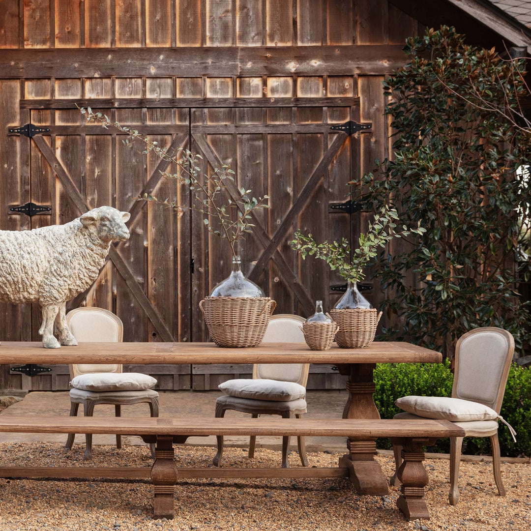 Vintage Farmhouse Harvest Dining Table set in rustic outdoor barn setting with chairs, wicker baskets, and sheep statue