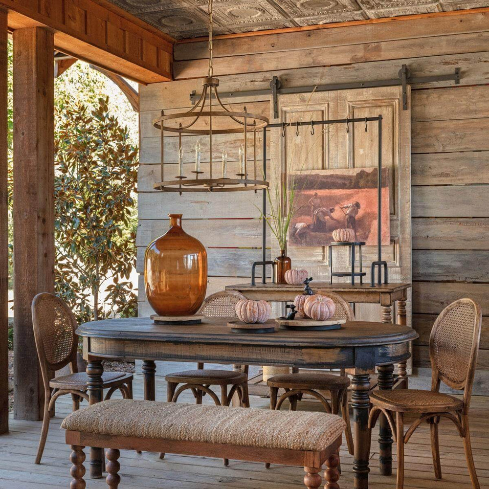 Rustic farmhouse dining area with wooden table, wicker chairs, and amber glassware in a vintage-style setting.