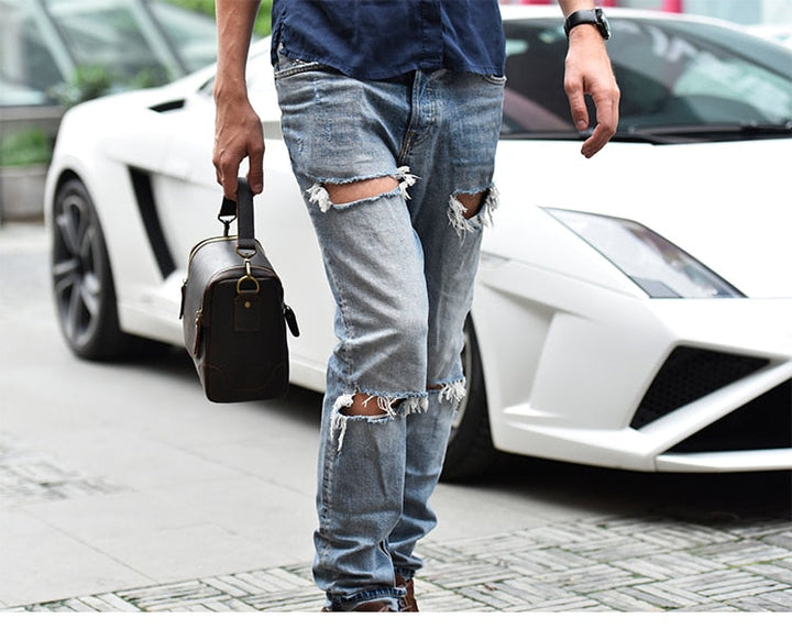 Man holding Vintage Full-Grain Leather Camera Bag walking by a white sports car.
