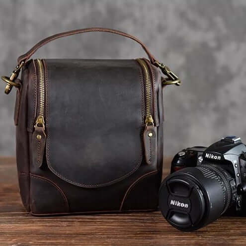 Vintage Full-Grain Leather Camera Bag with handle and zippers next to a Nikon camera on a wooden surface.