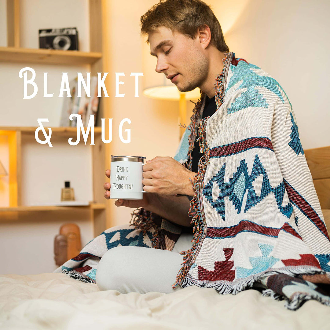 Man wrapped in patterned blanket holding 'Drink Happy Thoughts' mug in cozy room.