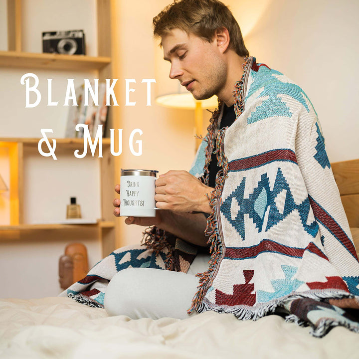 Man wrapped in patterned blanket holding 'Drink Happy Thoughts' mug in cozy room.