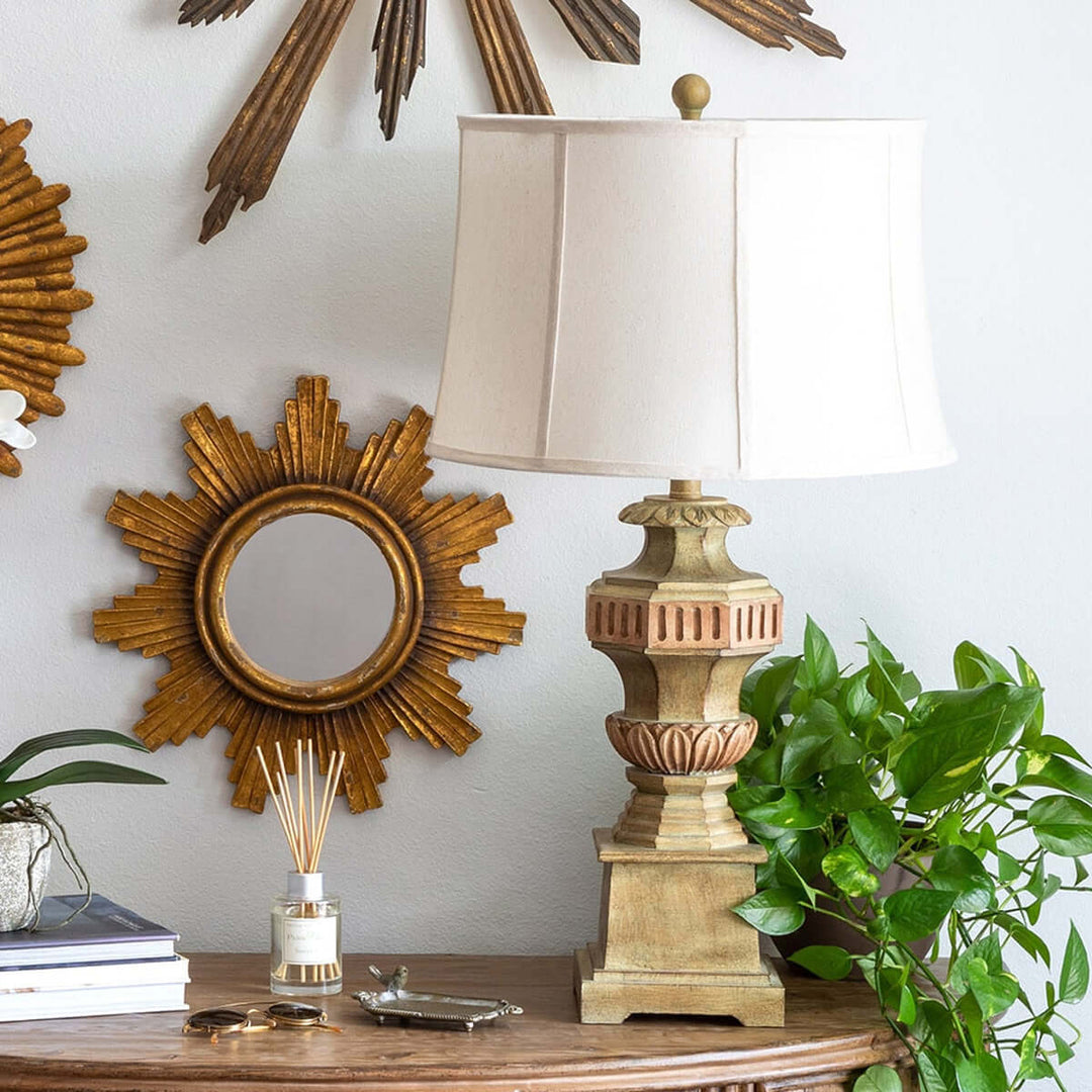 Vintage Greek Column Table Lamp on wooden table beside sunburst mirror and green plant