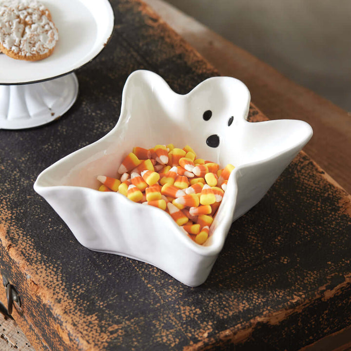 Vintage Halloween ghost candy dish in porcelain, filled with colorful candy corn, on a wooden table.