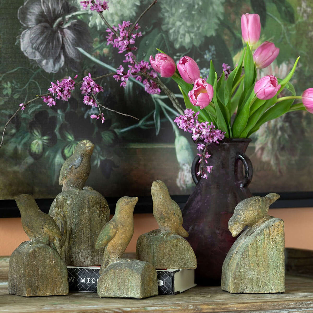 Set of 5 vintage-inspired bird figurines with aged finish next to pink flowers in a vase.