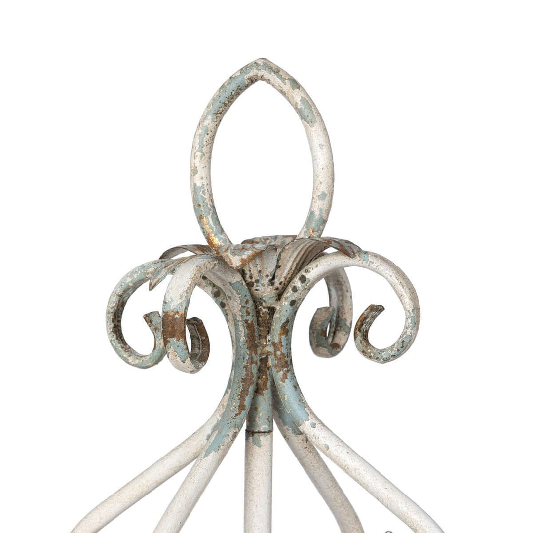 Close-up of a vintage tabletop chandelier's distressed white iron frame with elegant scrollwork detail.