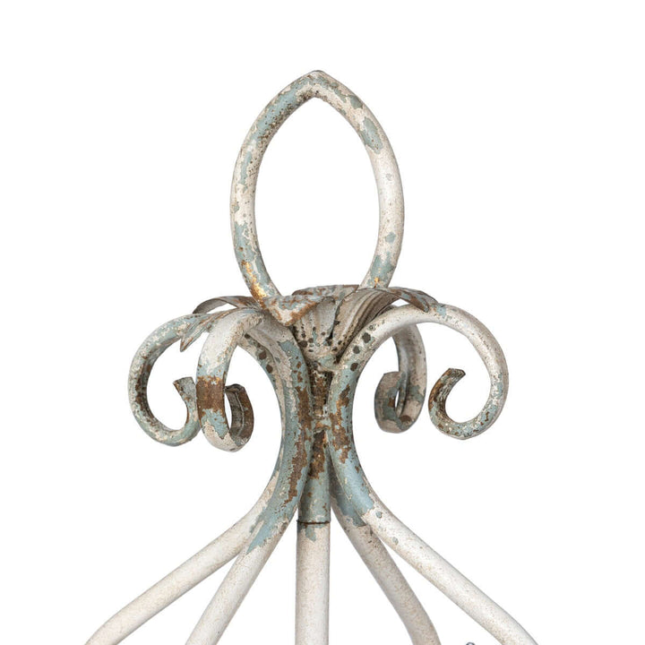 Close-up of a vintage tabletop chandelier's distressed white iron frame with elegant scrollwork detail.