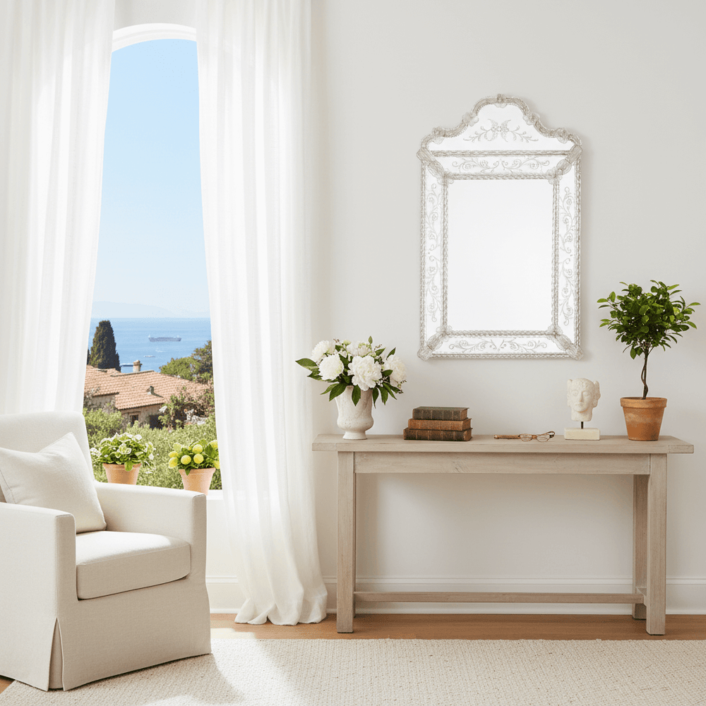 Living room with a white armchair, table with decor items, and a large Murano glass mirror on the wall.