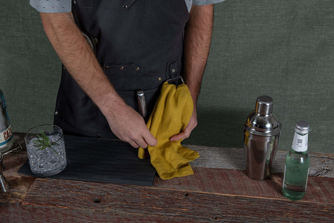 Bartender using Waxed Canvas Bartender Apron and Tools at wooden bar with drink and shaker
