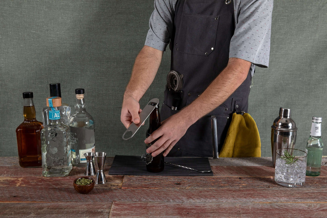 Bartender wearing Waxed Canvas Bartender Apron and Tools setup for mixology with various liquors and mixers on the table