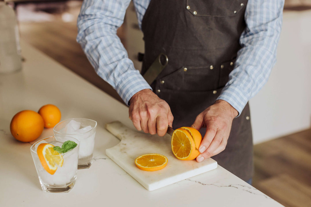 Man slicing an orange while wearing Waxed Canvas Bartender Apron and Tools in a kitchen setting