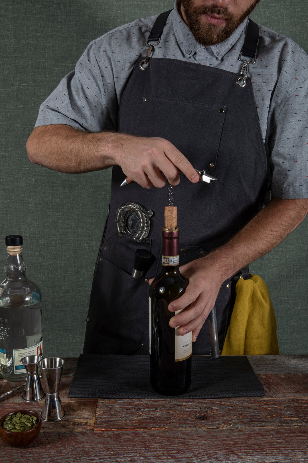 Bartender using Waxed Canvas Bartender Apron and Tools to open wine bottle on wooden counter