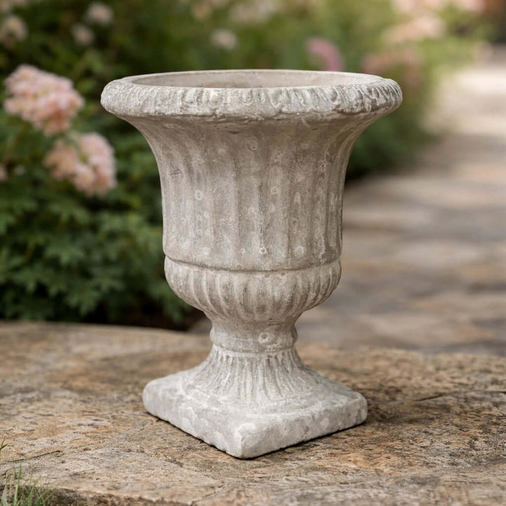 Empty Weathered Cement Pedestal Urn Planter in a garden setting