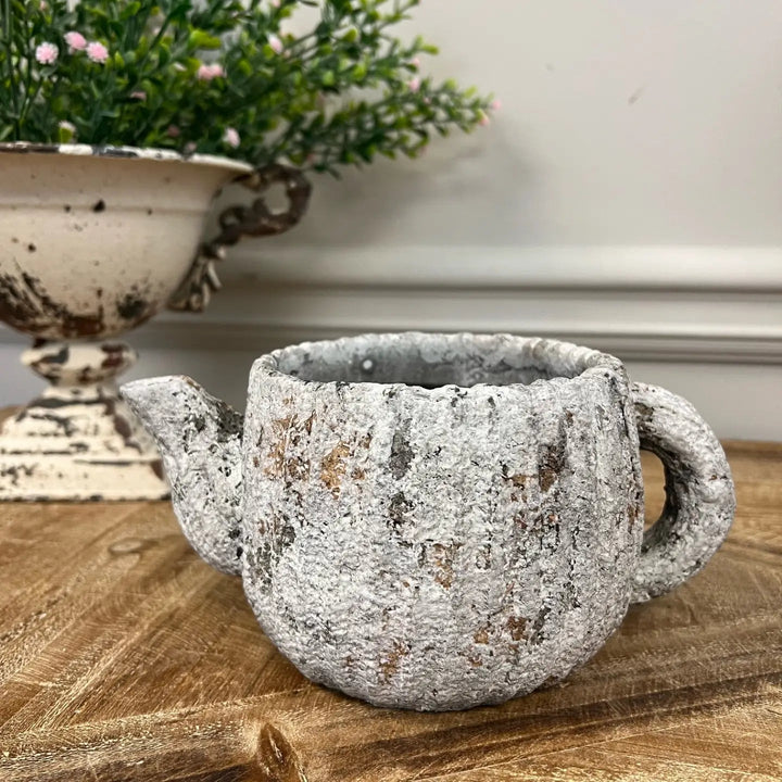 Rustic teapot planter styled on a garden shelf
