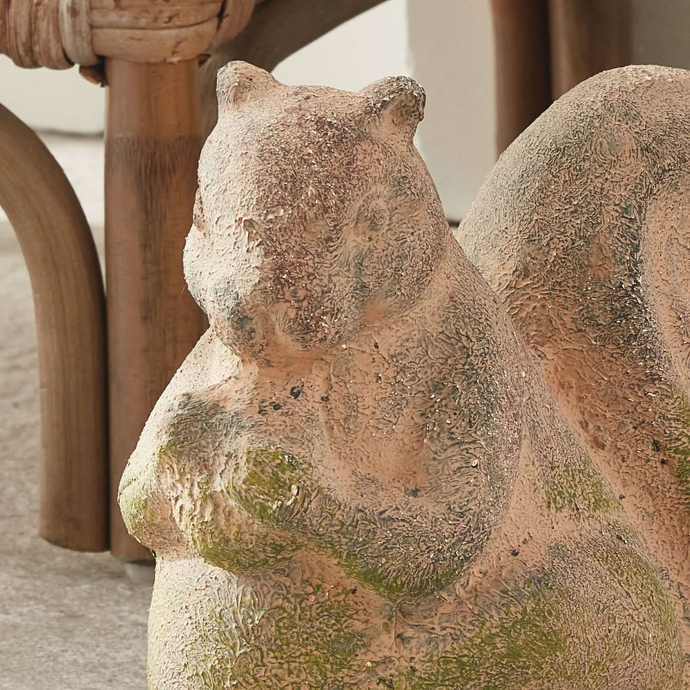 Weathered moss terracotta squirrel garden statue adding charm to outdoor decor.