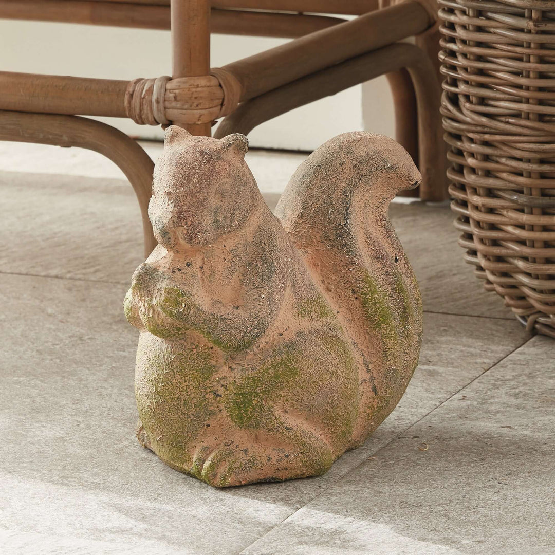 Weathered moss terracotta squirrel garden statue adding charm to outdoor space, detailed and whimsical home decor piece.