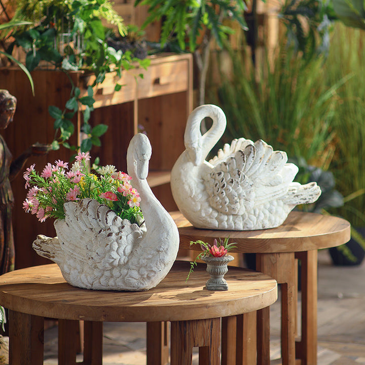 Weathered Swan Garden Planters filled with pink flowers on wood tables