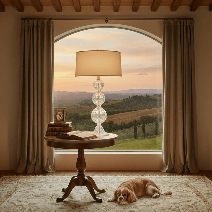 Cozy room with a lamp, table, open book, and dog in front of a large window with a scenic view.