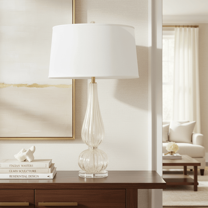 Table lamp with a white shade on a wooden table in a living room setting.