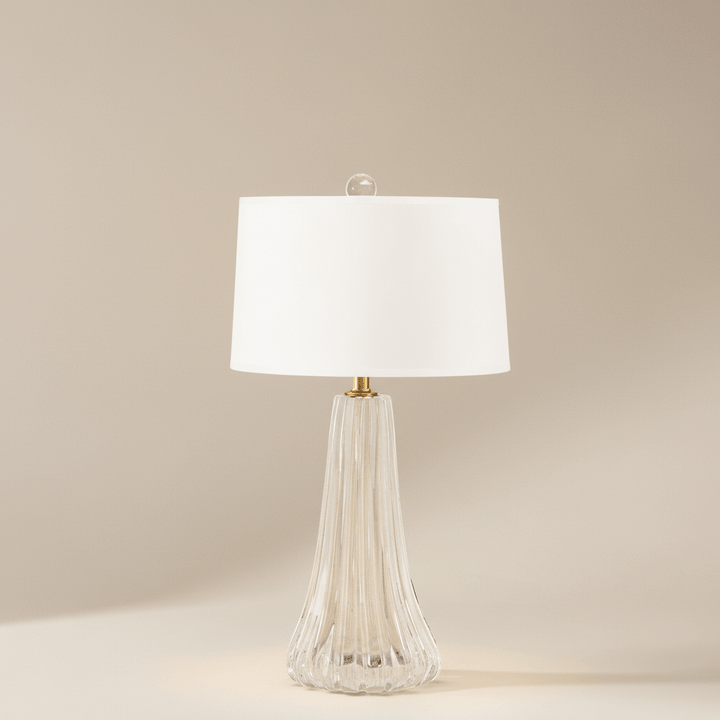 Table lamp with a white shade and ribbed glass base on a beige background