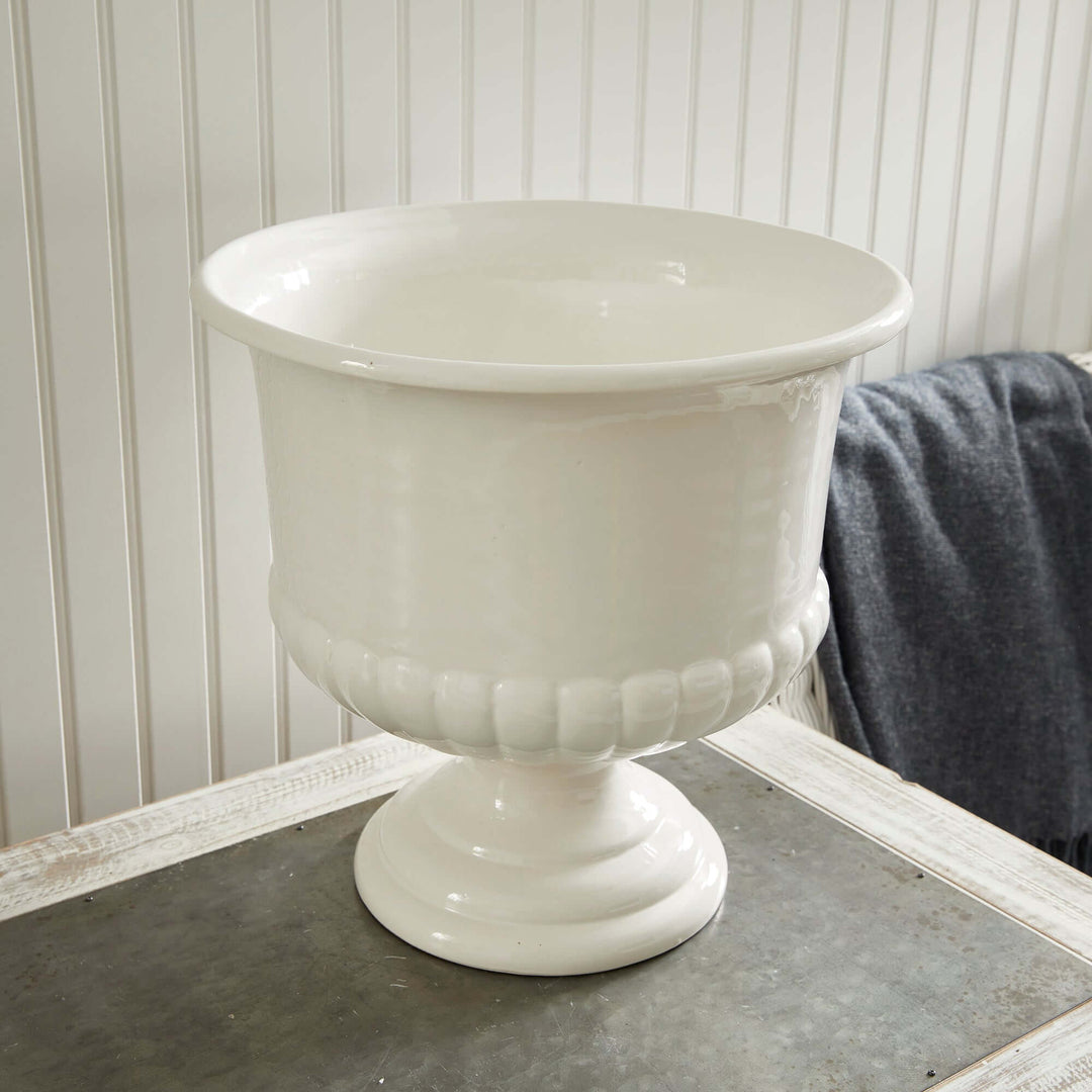 White ceramic urn planter with flared rim and pedestal base, perfect for Tuscan-inspired decor.